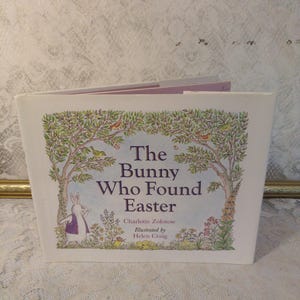 May include: A children's book titled "The Bunny Who Found Easter" by Charlotte Zolotow, illustrated by Helen Craig. The cover features a white bunny in a purple vest, trees, birds, and flowers. The book is open, revealing the inside pages.