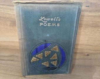 May include: A hardcover book titled Lowell's POEMS with a dark green cover. The front features a circular cutout revealing a deep purple fabric inlay, decorated with a gold-toned geometric design of triangular shapes and curved lines.