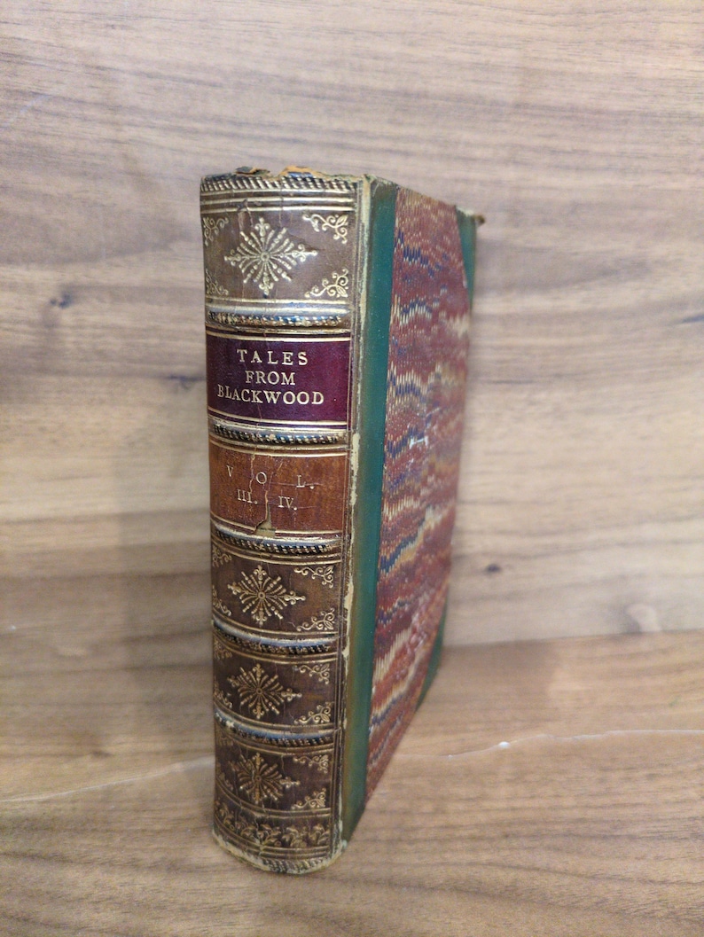 May include: A hardcover book titled Tales from Blackwood Vol. III. IV. featuring a brown leather spine with gold embossed floral patterns and lettering, and a marbled cover with green, red, and blue patterns on the side and back panels.