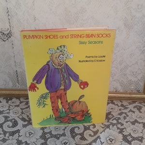 May include: A yellow book cover with a cartoon scarecrow wearing a purple jacket, brown pants, and a green hat. The book title is "Pumpkin Shoes and String Bean Socks: Sissy Seasons".