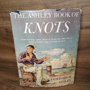 May include: Vintage book titled "The Ashley Book of Knots." The cover features an illustration of a sailor with a pipe, demonstrating knots. The book's title is in large, white letters against a blue and gray background.