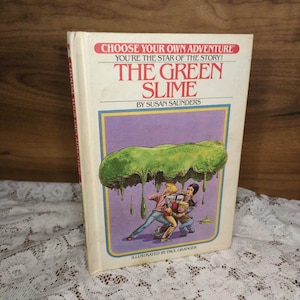 May include: A vintage paperback book titled "The Green Slime" from the "Choose Your Own Adventure" series. The cover features an illustration of children under a dripping green slime. The book is by Susan Saunders and illustrated by Paul Granger.