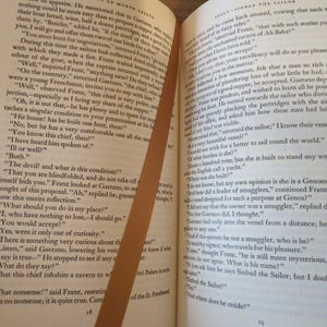 May include: Open book with text from "The Count of Monte Cristo" and "Sinbad the Sailor." A brown bookmark diagonally crosses the pages. The pages are yellowed with age.