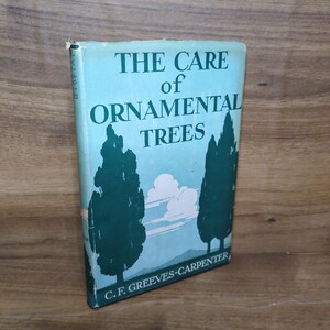 May include: A hardcover book titled The Care of Ornamental Trees by C. F. Greeves-Carpenter. The dust jacket features a light blue background with dark green silhouettes of two tall trees, white clouds, and dark green text on the front cover.