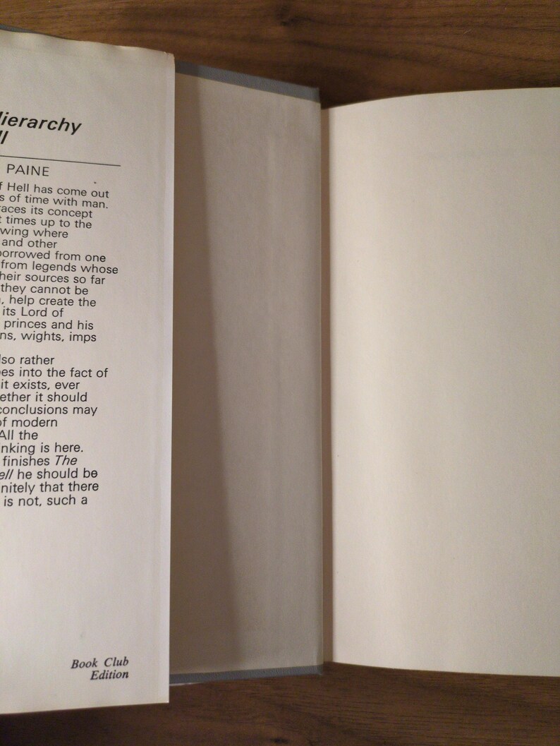 May include: An open book with text on the left page and a blank right page. The book is a "Book Club Edition". The pages are off-white, and the spine is light grey. The book is on a wooden surface.