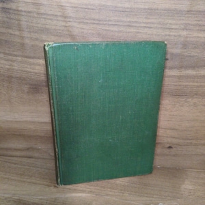 May include: A hardcover book with a textured, dark green cover. The book is standing upright, with the spine visible. The edges of the cover show slight wear. The background is a wooden surface.