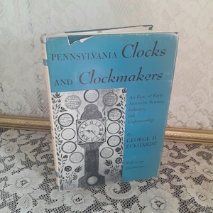 May include: A blue book titled "Pennsylvania Clocks and Clockmakers: An Epic of Early American Science, Industry, and Craftsmanship" by George H. Eckhardt. The book cover features a black and white illustration of a clock with many smaller clocks surrounding it.