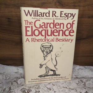 May include: A vintage book titled "The Garden of Eloquence" by Willard R. Espy. The cover features a lion illustration in a suit and the subtitle "A Rhetorical Bestiary". The book is on a white lace surface.