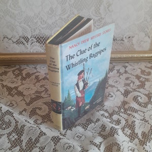May include: A yellow and black hardcover book titled "The Clue of the Whistling Bagpipes" with a Nancy Drew Mystery Stories logo. The cover features an illustration of a young person in a kilt playing bagpipes.
