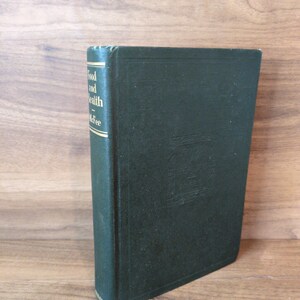 May include: A dark green hardcover book titled "Food and Health" by McFee. The book is standing upright on a wooden surface. The spine of the book is visible, with gold lettering. The book's cover has a textured appearance.