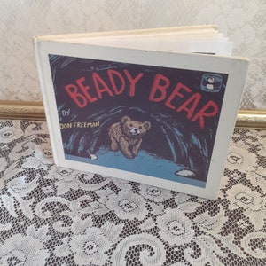 May include: A white book with a blue cover featuring the title "Beady Bear" by Don Freeman. The cover illustration shows a brown bear cub peeking out of a cave.