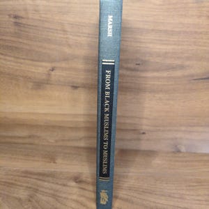 May include: A hardcover book titled "FROM BLACK MUSLIMS TO MUSLIMS" by Marsh. The book has a teal cover with gold lettering and a decorative emblem at the bottom. The spine is visible, showing the title and author.