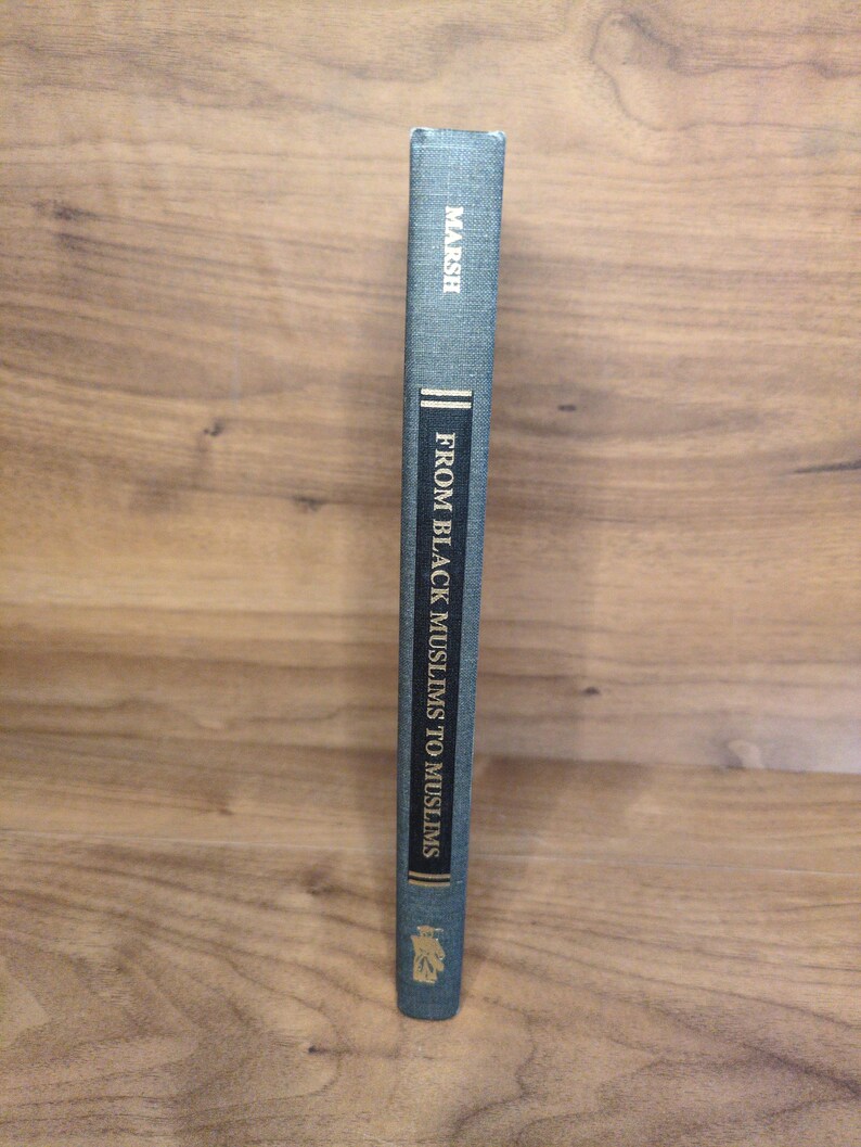 May include: A hardcover book titled "FROM BLACK MUSLIMS TO MUSLIMS" by Marsh. The book has a teal cover with gold lettering and a decorative emblem at the bottom. The spine is visible, showing the title and author.