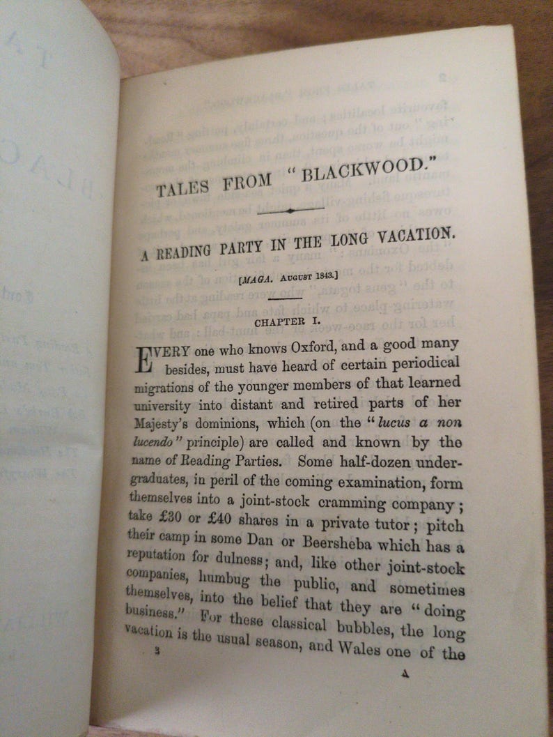 May include: An open book page featuring the title TALES FROM BLACKWOOD and the chapter heading A READING PARTY IN THE LONG VACATION. The text begins with the letter E and discusses university students forming a joint-stock cramming company.