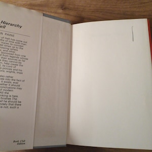 May include: An open book with white pages. The left page displays text from "Hierarchy Hell" by Paine. The right page is blank, marked with a single vertical line. The book is a "Book Club Edition".