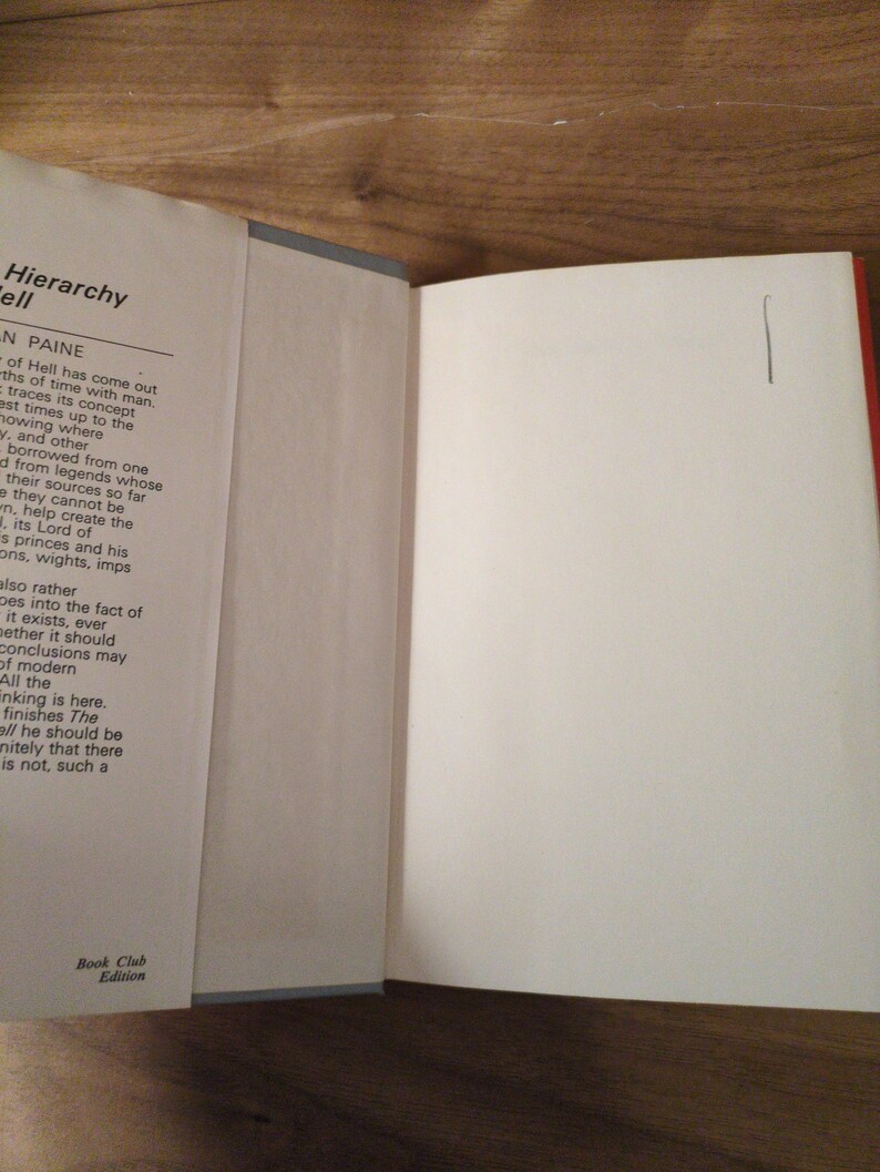 May include: An open book with white pages. The left page displays text from "Hierarchy Hell" by Paine. The right page is blank, marked with a single vertical line. The book is a "Book Club Edition".