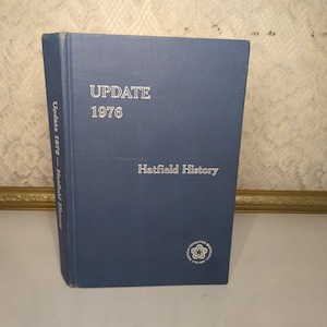 May include: A blue hardcover book titled "UPDATE 1976 Hatfield History." The book has white lettering and a small emblem on the bottom right corner. The spine reads "Update 1976 - Hatfield History."