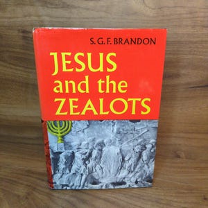 May include: A book titled "JESUS and the ZEALOTS" by S.G.F. Brandon. The cover is predominantly red with yellow lettering. The lower portion of the cover features a black and white image of a historical scene with figures and a menorah.