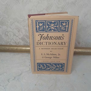 May include: A tan-colored book with a blue and white design on the cover. The title is "Johnson's Dictionary" with the subtitle "A Modern Selection" by "E. L. McAdam, Jr. & George Milne".