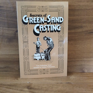 May include: A book titled "Secrets of Green-Sand Casting" with a beige cover. The cover features black and white illustrations of two figures working with metal. The text is in a bold, stylized font.