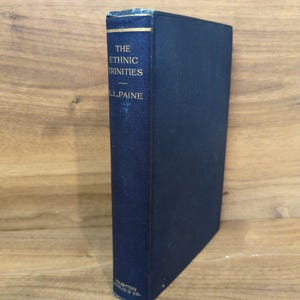 May include: A hardcover book titled "The Ethnic Trinities" by L.L. Paine. The book has a dark blue cover with gold lettering and a gold band at the top. The book is standing upright.