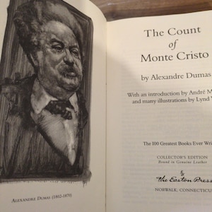 May include: Open book with the title "The Count of Monte Cristo" by Alexandre Dumas. Features a portrait of Alexandre Dumas and text indicating it's a Collector's Edition bound in genuine leather from The Easton Press.