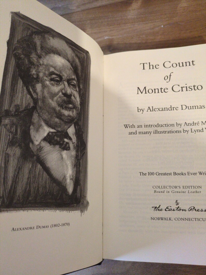 May include: Open book with the title "The Count of Monte Cristo" by Alexandre Dumas. Features a portrait of Alexandre Dumas and text indicating it's a Collector's Edition bound in genuine leather from The Easton Press.