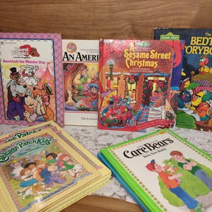 May include: A collection of vintage children's books, including titles like "Pound Puppies," "Sesame Street Christmas," and "Care Bears." The books feature colorful illustrations and are stacked on a wooden surface.