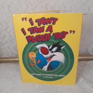 May include: A yellow book with a green and blue circle on the cover. The circle features a cartoon cat and bird. The book title is "I TAWT I TAW A PUDDY TAT". The book is titled "Fifty Years of Sylvester and Tweety" by Jerry Beck.