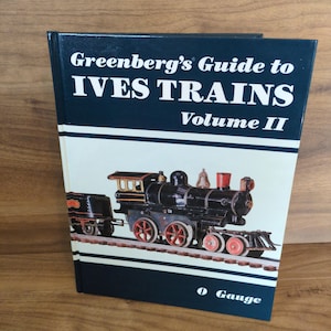 May include: A hardcover book titled "Greenberg's Guide to IVES TRAINS Volume II" with a navy blue cover and a detailed illustration of a black and red toy train. The book is labeled "O Gauge".