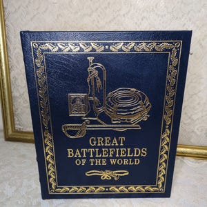 May include: A hardcover book titled "Great Battlefields of the World." The book has a dark blue cover with gold embossed illustrations and text. The cover features a decorative border and military-themed imagery.