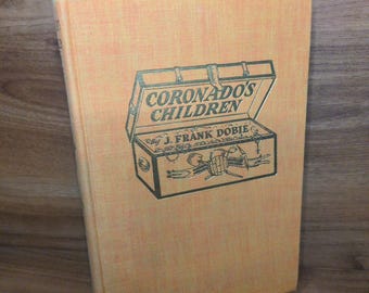 May include: A hardcover book with a textured light orange cover. The front cover features a dark green illustration of an open chest containing various tools and the text "CORONADO'S CHILDREN" and "By J. FRANK DOBIE" printed in dark green.