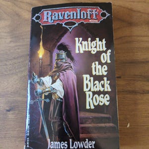 Puede incluir: Un libro de bolsillo titulado "Knight of the Black Rose" de James Lowder. La portada muestra un caballero con armadura y espada, con una capa morada oscura. El fondo muestra una antorcha y escaleras de piedra. Serie Ravenloft.