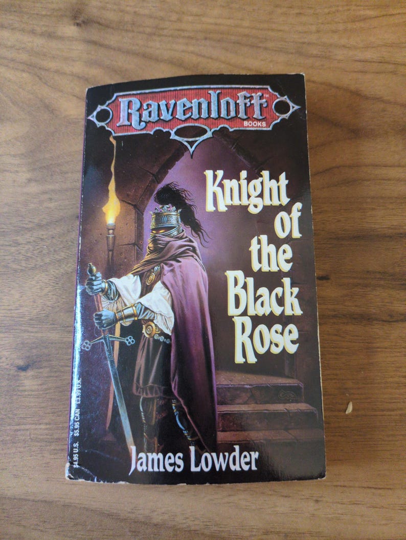 Puede incluir: Un libro de bolsillo titulado "Knight of the Black Rose" de James Lowder. La portada muestra un caballero con armadura y espada, con una capa morada oscura. El fondo muestra una antorcha y escaleras de piedra. Serie Ravenloft.