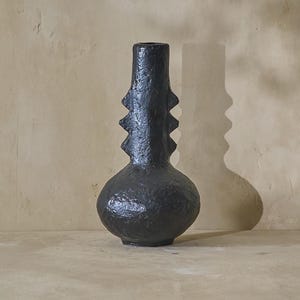 May include: Black ceramic vase with a textured surface and a unique, geometric design. The vase has a wide base and a narrow neck.