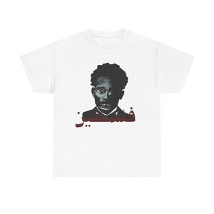Peut inclure: T-shirt blanc avec un motif noir et rouge représentant un visage et du texte arabe. Le design est artistique et stylisé. Le t-shirt est fait d'un tissu doux et confortable.