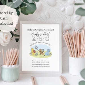 May include: A framed print with the text "Help Us Create a Keepsake! Baby's First A.B.C Book & Word Adventures" featuring Winnie the Pooh characters. Pencils are in small white and light green ceramic pots. The words "Activity Sign Included" are in a white circle.