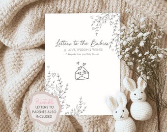 May include: A white card with the text "Letters to the Babies of LOVE, WISDOM & WISHES" and floral illustrations. The card is a keepsake from a baby shower. Two white crochet bunnies and a sprig of white flowers are next to the card.