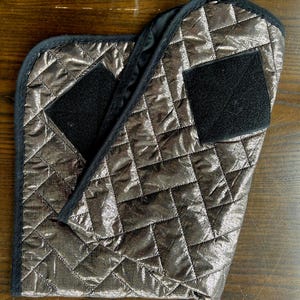 May include: A silver quilted fabric with black velcro patches. The fabric is folded in half.