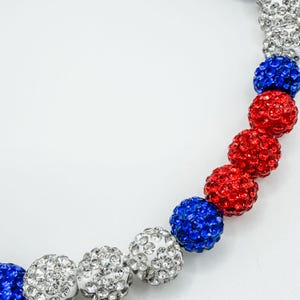 May include: A beaded bracelet with alternating red, white, and blue crystal balls. The bracelet is made of small, sparkly crystals.