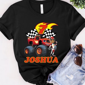 May include: Black t-shirt with a red monster truck and a cartoon character. The truck has a checkered flag and the text "Joshua" is printed on the shirt.