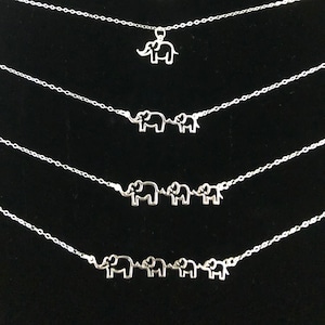 May include: Five silver necklaces with elephant pendant charms. The necklaces are layered on a black background. The elephants are different sizes and some are connected to each other.