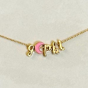 May include: A delicate gold-colored necklace with the letters "g p h l" in a cursive font. The letters are in gold and are connected by a thin gold chain. A pink circular charm is between the "g" and the "p".