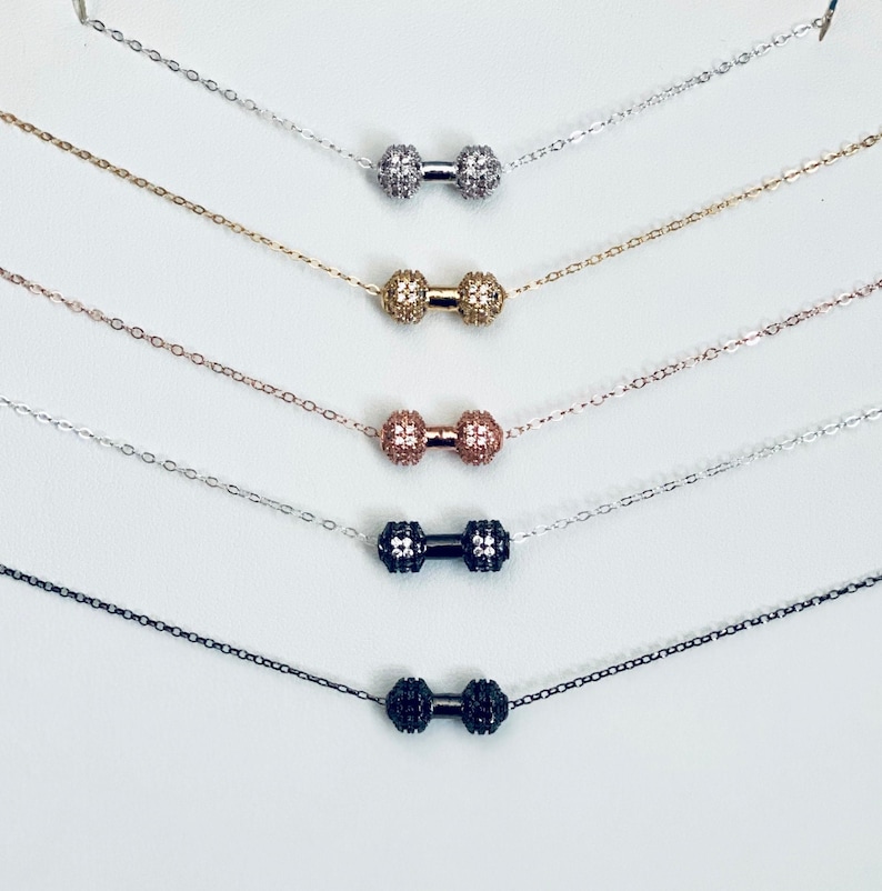 Peut inclure: Cinq colliers d&eacute;licats avec des pendentifs en forme d'halt&egrave;res. Les pendentifs sont en argent, or, or rose, noir et blanc. Chaque pendentif est orn&eacute; de pierres de zircone cubique scintillantes.