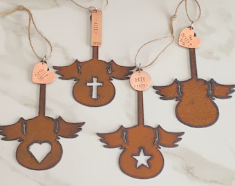May include: Four rustic metal angel ornaments with copper heart, cross, star, and circle cutouts. Each ornament has a copper tag with a name and year. The tags read "July 2020", "Alex 2020", "Greg 2020", and "The Bucketts 2020".