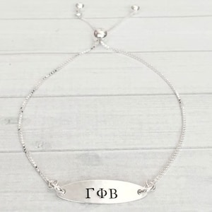 May include: A silver adjustable bracelet with a silver oval charm that says "ΓΦΒ".