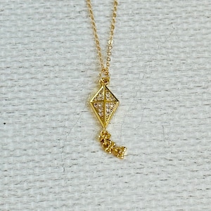 May include: A gold necklace with a diamond-encrusted kite pendant and a dangling chain of small charms.