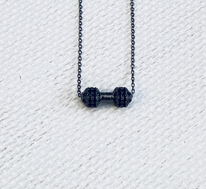 Peut inclure: Un collier &agrave; cha&icirc;ne noire avec un petit pendentif halt&egrave;re noir. L'halt&egrave;re est recouvert de petites pierres noires.