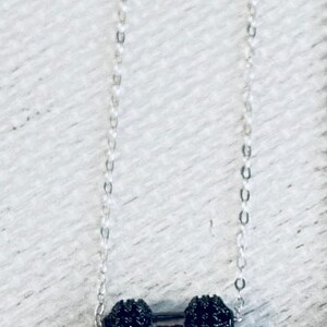Peut inclure: Un collier en cha&icirc;ne argent avec deux pendentifs ronds noirs perl&eacute;s reli&eacute;s par une barre argent&eacute;e.