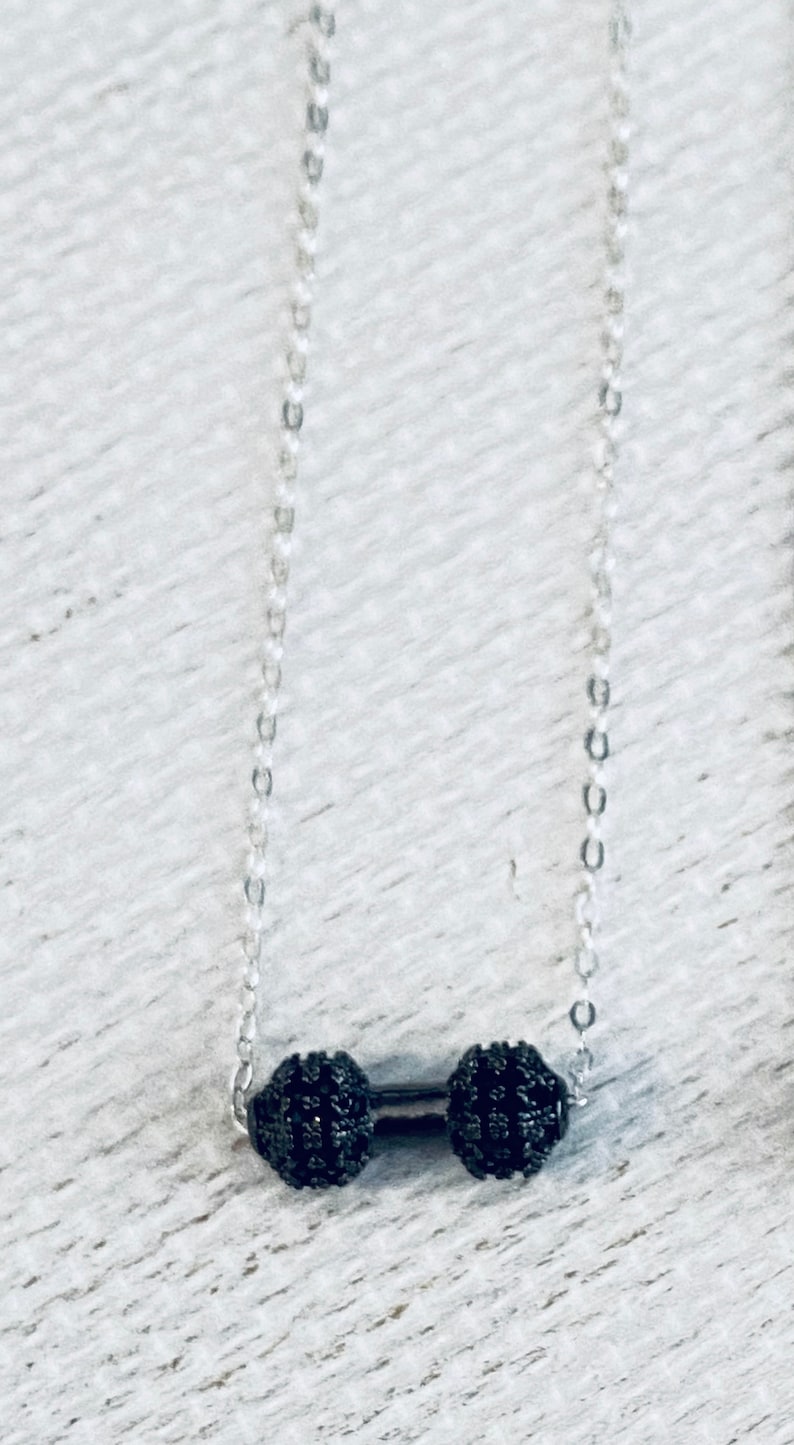 Peut inclure: Un collier en cha&icirc;ne argent avec deux pendentifs ronds noirs perl&eacute;s reli&eacute;s par une barre argent&eacute;e.